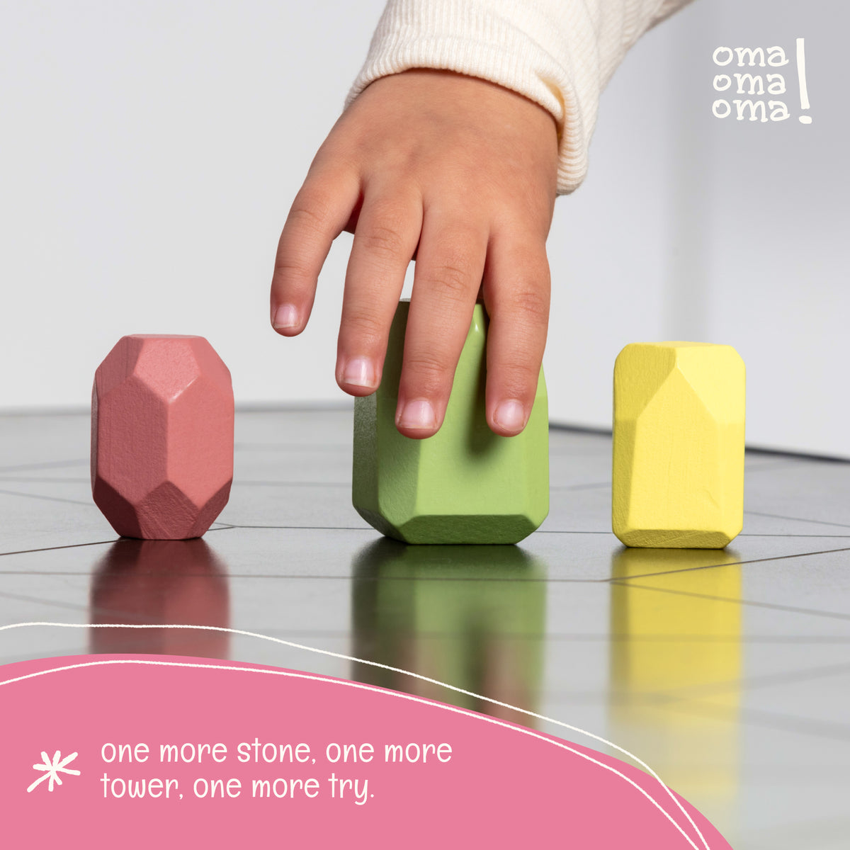 Toddler hand next to OmaOmaOma wooden balance stones showing three graduated sizes — large, medium, small